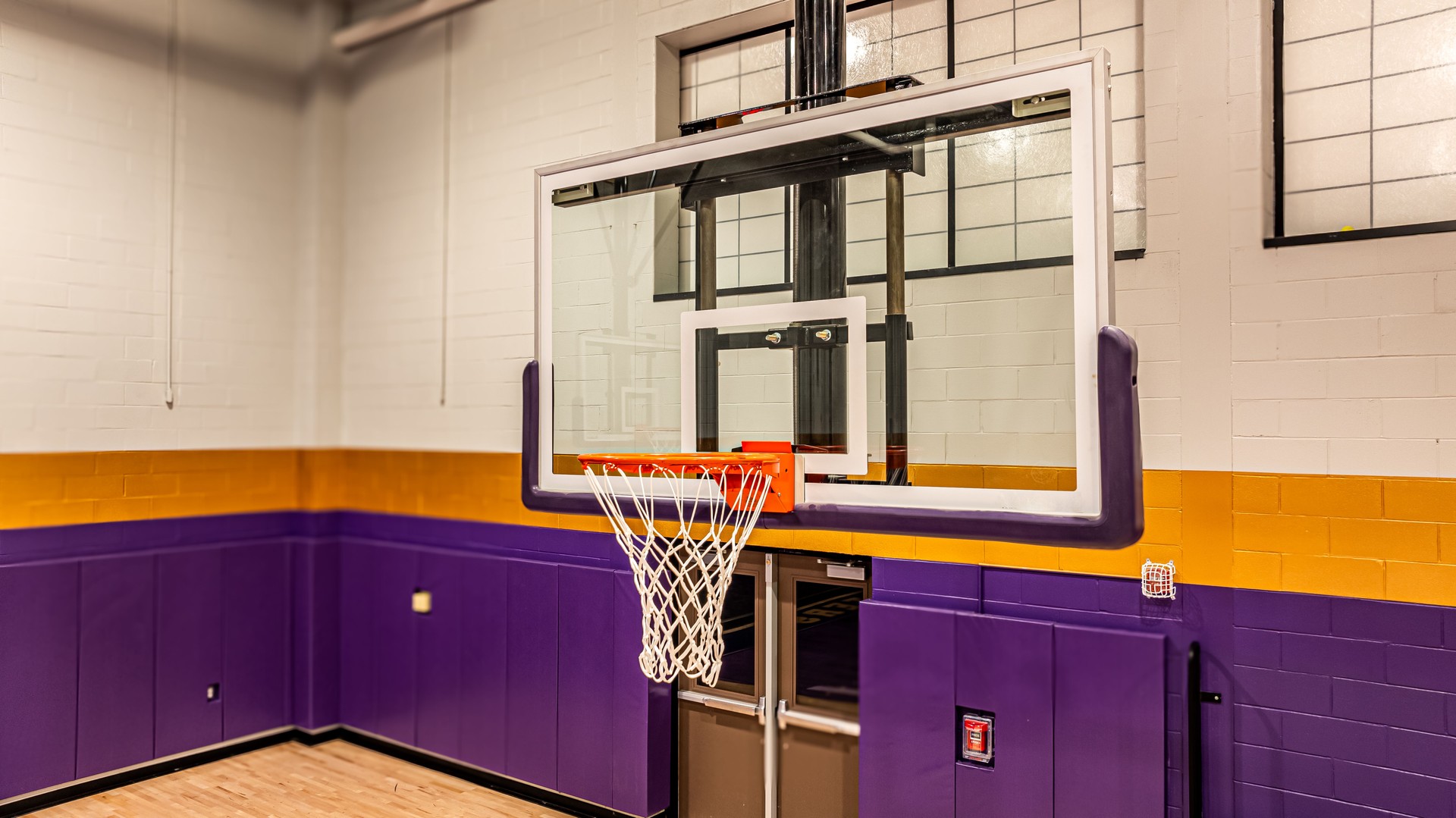 New ceiling mounted basketball hoop with clear glass, acrylic backboard, in a indoor school gym.